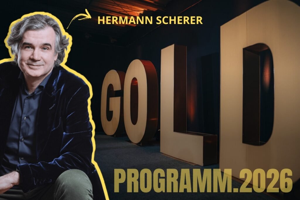 Promobild zum Gold Programm 2026 mit einem lächelnden Mann im Vordergrund und großen beleuchteten GOLD-Buchstaben im Hintergrund. Oben zeigt ein gelber Textpfeil auf den Mann mit der Aufschrift ‚Hermann Scherer‘, unten steht ‚Programm 2026